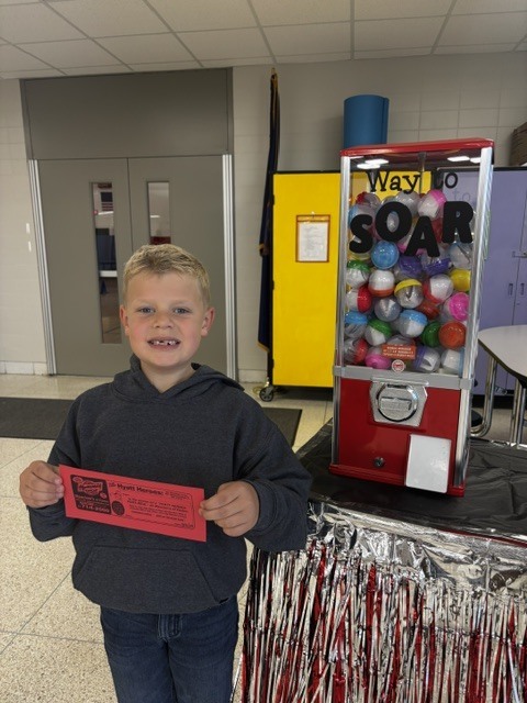 A smiling student holding a red prize ticket in front of a red prize capsule machine.