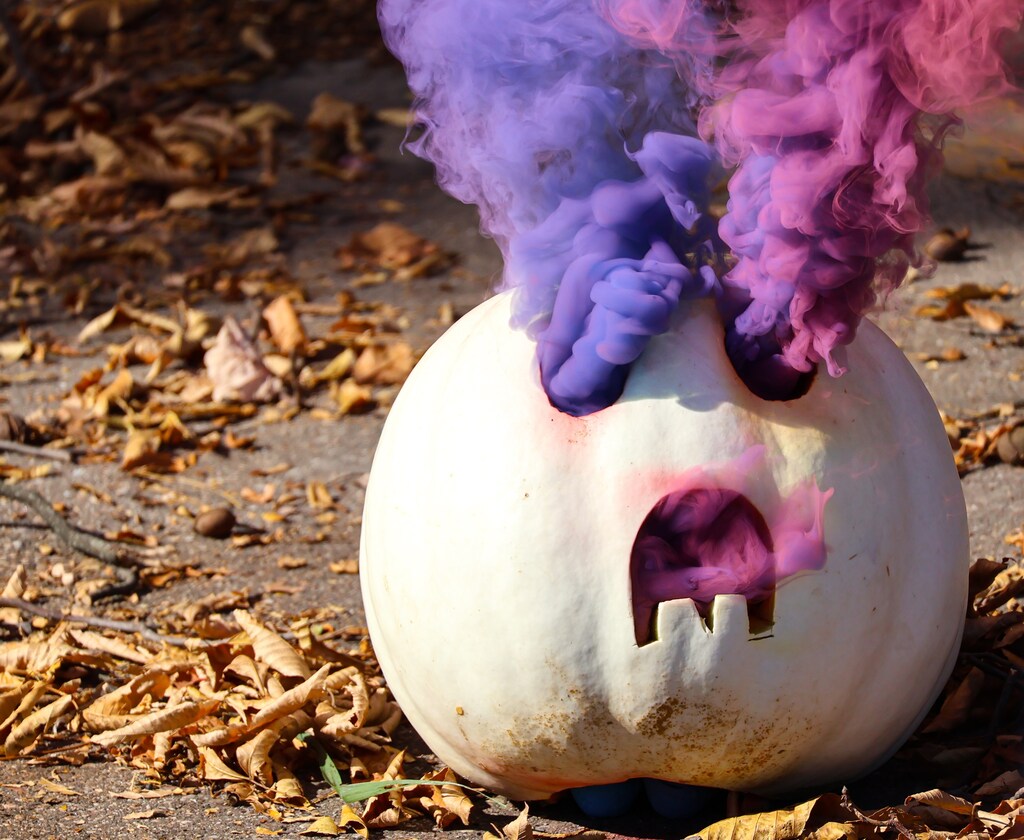 white pumpkin with purple and pink smoke and leaves in background