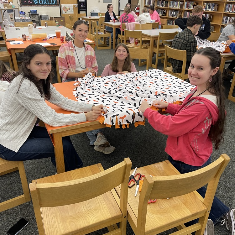 students sitting at a table, making a blanket for animals