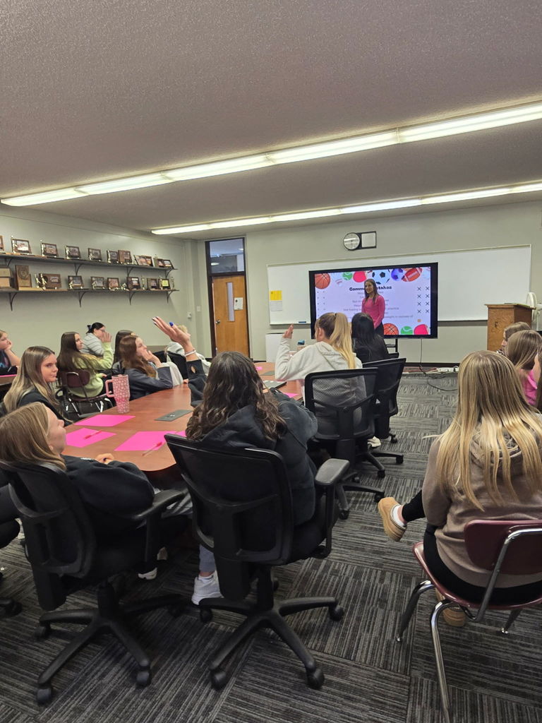 Group of HS girls around table, presentor at the front