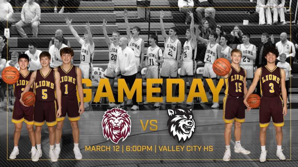 Photo of the Linton-HMB Lions boys basketball team standing along the bench during a game with several players raising their arms and cheering while coaches and teammates celebrate. Fans sit in the bleachers behind them as the team reacts to a play on the court