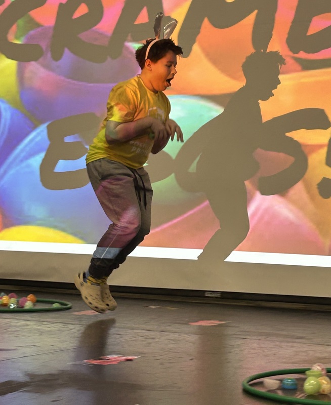 Student in bunny ears hopping like a rabbit in front of a festive easter background