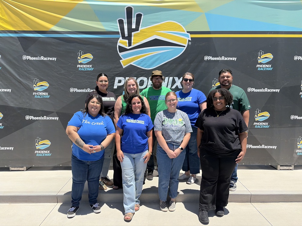 Photo shows teachers and staff in front of a Phoenix Raceway Backdrop