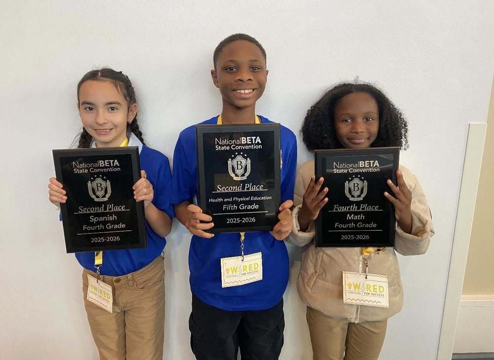 Three Terry Elementary students stand side by side against a white wall, each holding a black award plaque from the National Beta State Convention. The student on the left holds a plaque that reads “Second Place, Spanish, Fourth Grade, 2025–2026.” The student in the center holds a plaque that reads “Second Place, Health and Physical Education, Fifth Grade, 2025–2026.” The student on the right holds a plaque that reads “Fourth Place, Math, Fourth Grade, 2025–2026.” All three students are smiling and wearing school ID badges on yellow lanyards.