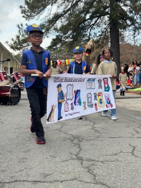 Children dressed as police officers and dogs holding a banner of the book Officer Buckle and Gloria.