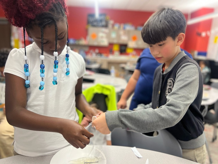 Two elementary students are working together to cut things 