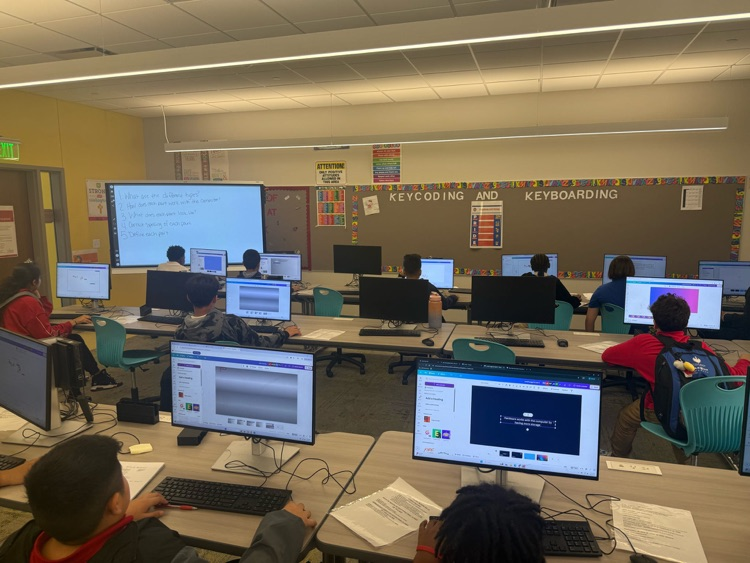 Students are actively working in the computer lab on computers 
