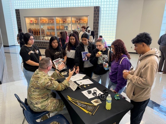 Several students stand around Army National recruiter as he talks about the benefits of joining 