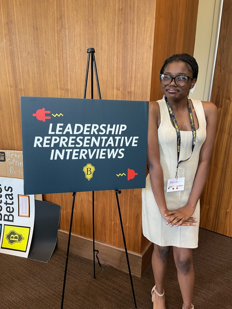 One of our students is standing next to her leadership sign