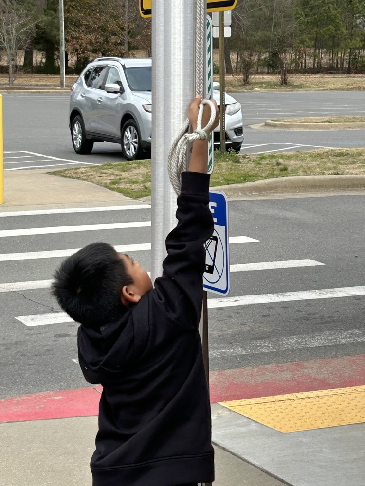 A student pulls the rope on a flagpole to help raise the American flag outside the school.