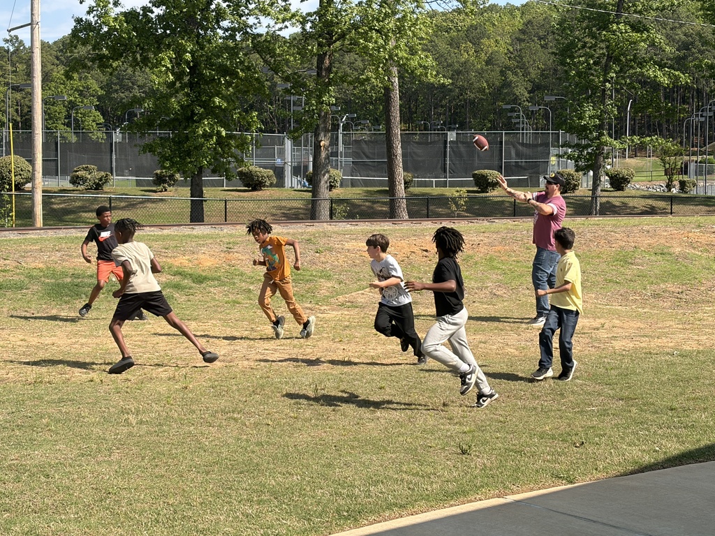 a group of students plays football with a grown up at the park