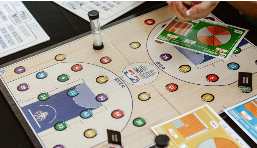 game board with numbers, an hour glass timer, a female's hand and the math hoops logo on the center of the board.