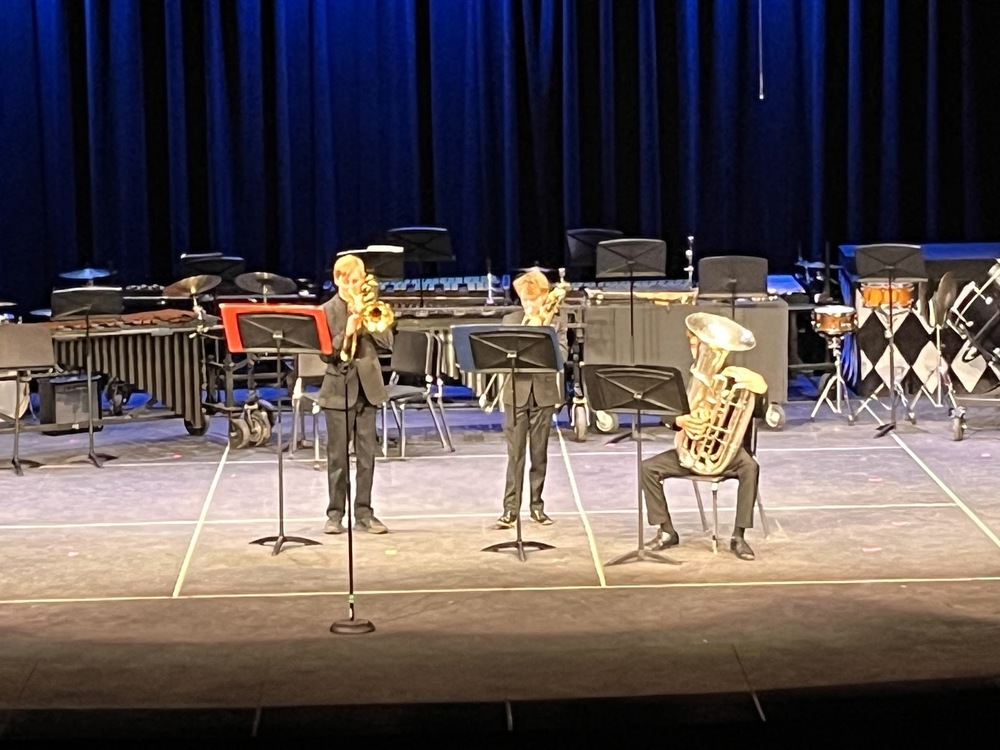 Three students playing musical instruments on stage.