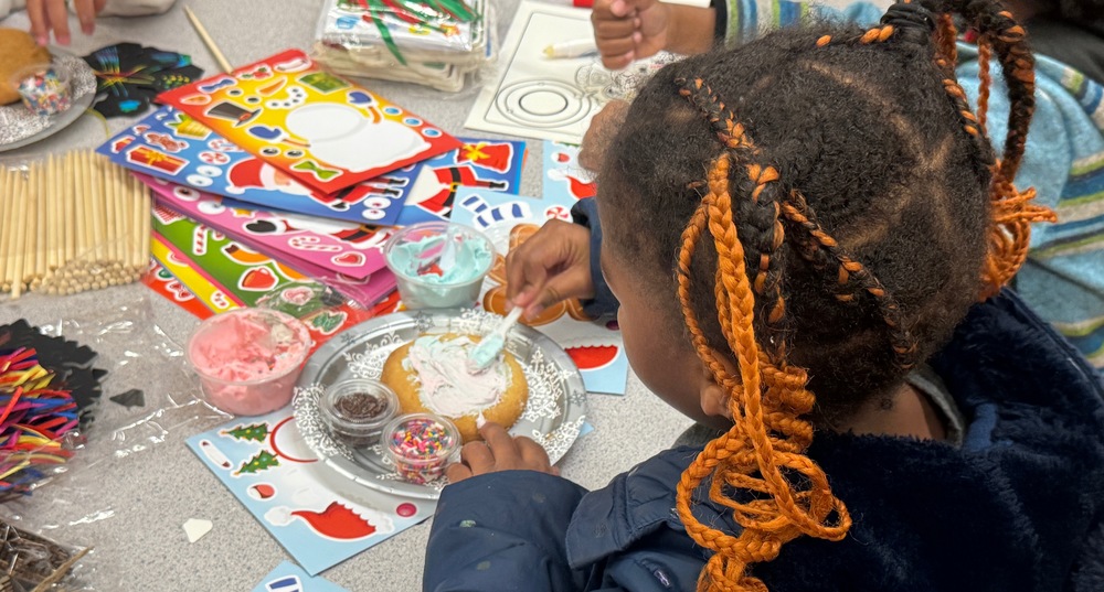 Village ECE student decorating sugar cookie with white frosting and colorful sprinkles
