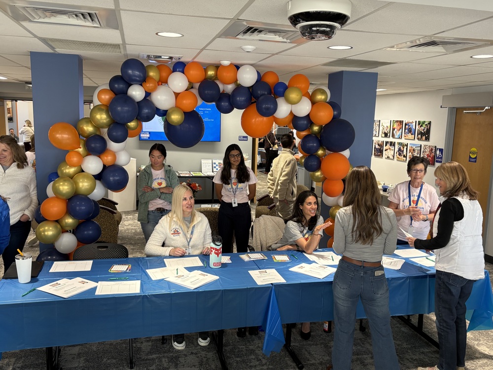 HR employees stand behind a registration table decorated with a large blue, orange, white, and gold balloon arch.
