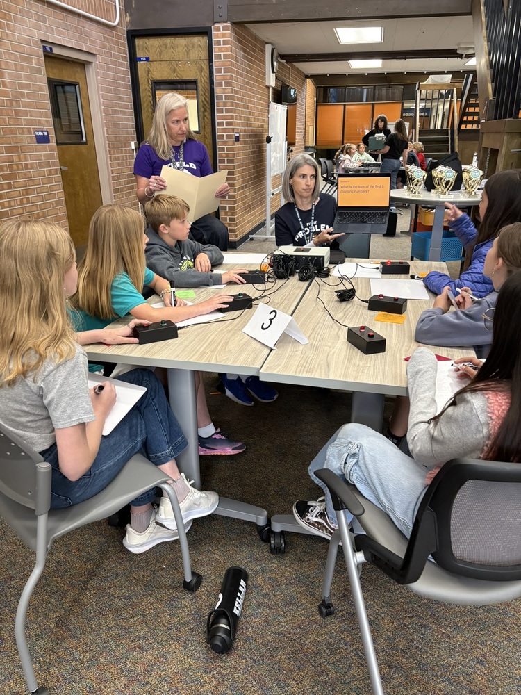 Mathletes participate in a buzzer round during a tournament with two teachers looking on.