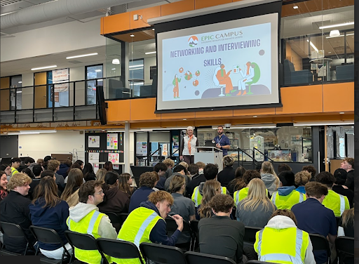 A large group of students in a modern atrium attends a presentation titled "Networking and Interviewing Skills."