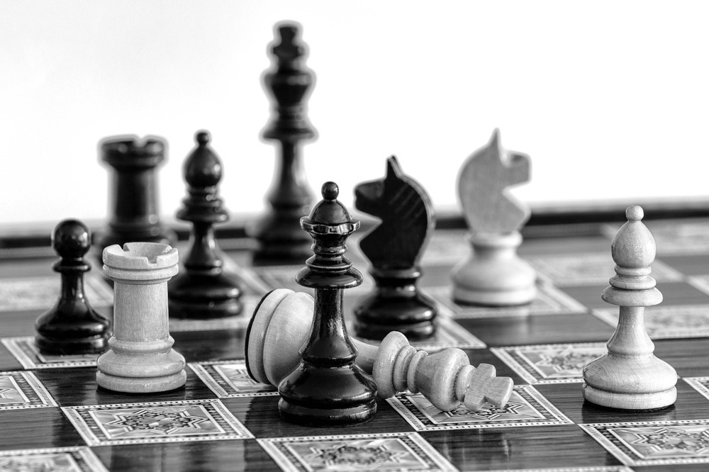 black and white photo of chess pieces, white king laying down