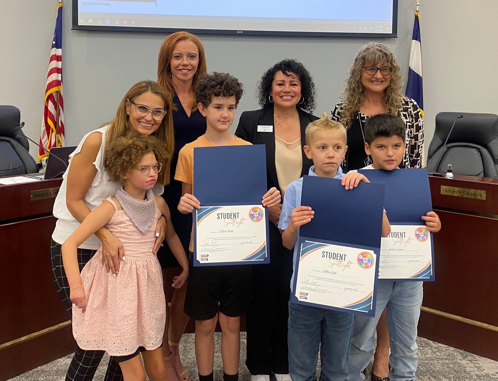 Four students and an adult stand with three Board of Education members. Three students hold up their Student Spotlight certificates. Setting is the LPS Boardroom.