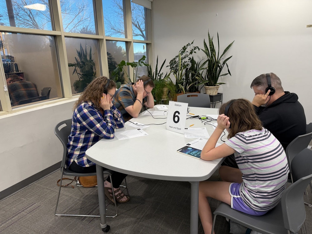 Four people wearing head phones sit at a table for a dyslexia simulation.