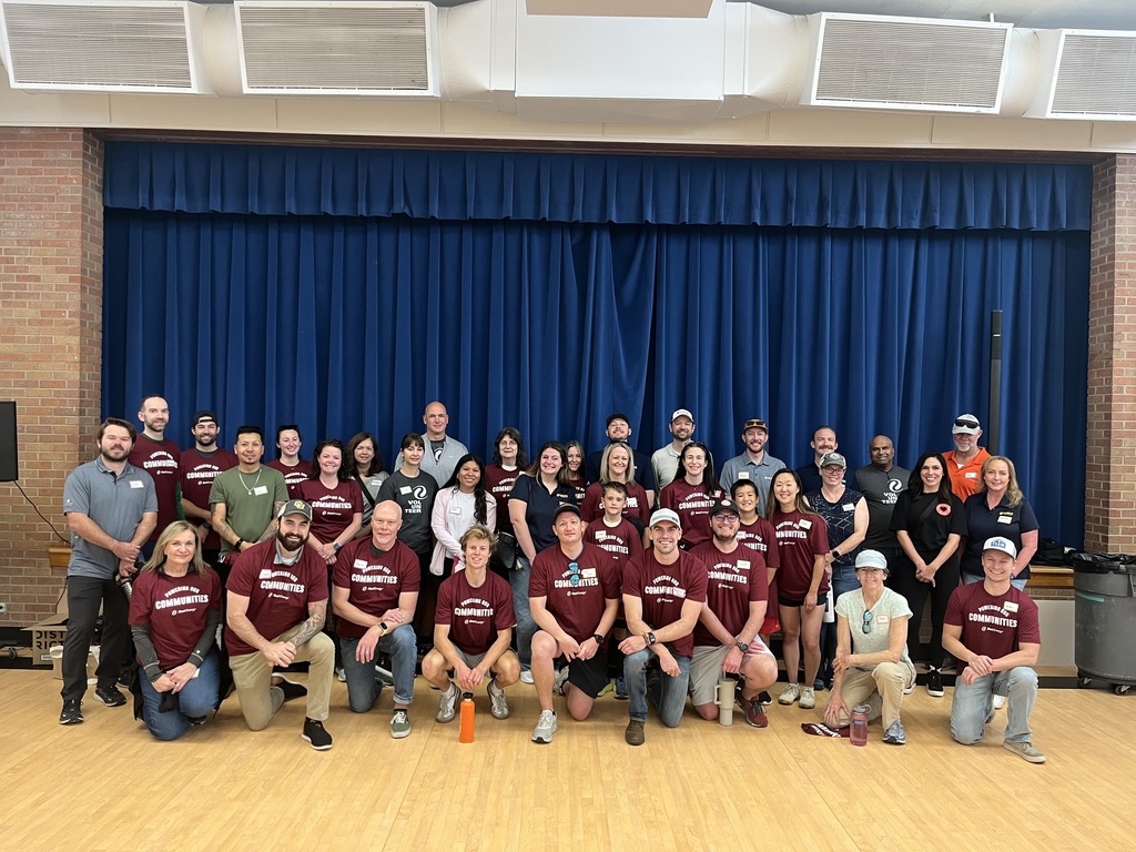 Group of about 35 people posing indoors, many wearing matching maroon “Communities” shirts.