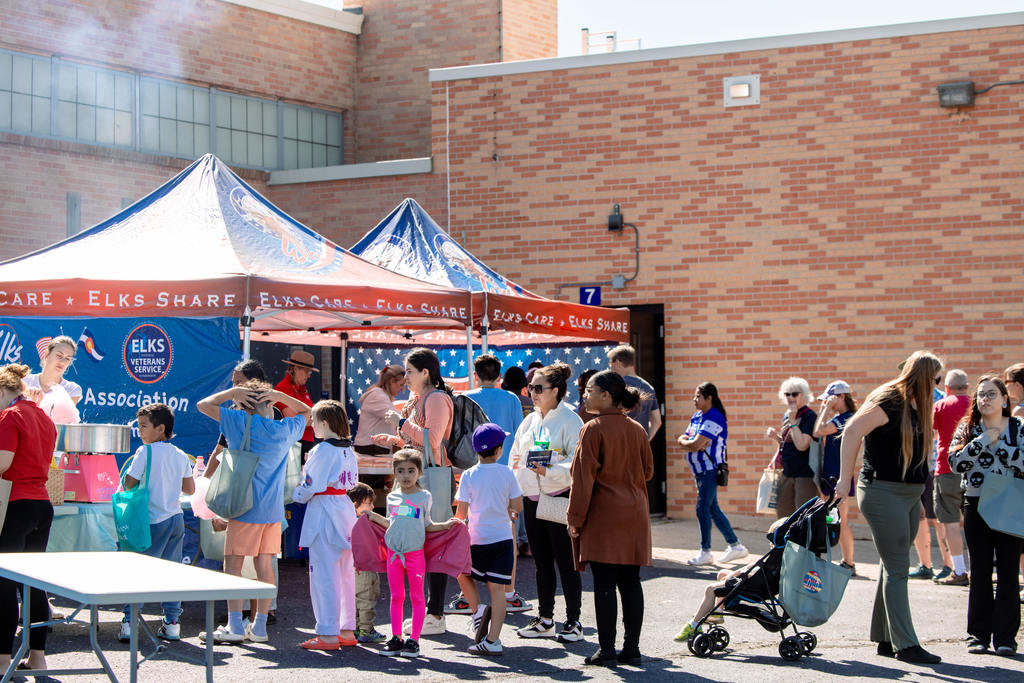 Families and children line up at the Littleton Elks Lodge tent during the East Community Center Community Resource Expo, where volunteers serve food and cotton candy.