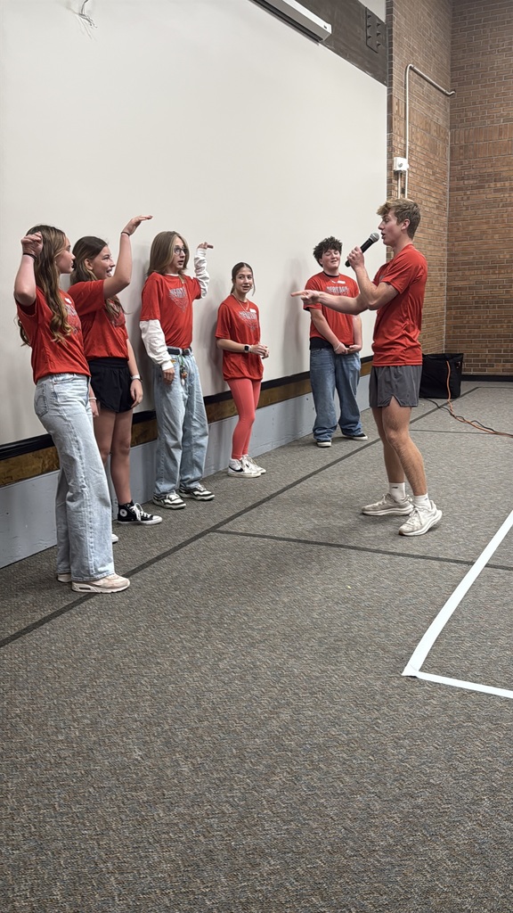 A group of 5 middle school students participates in an icebreaker activity led by a high school student. All are wearing red shirts.