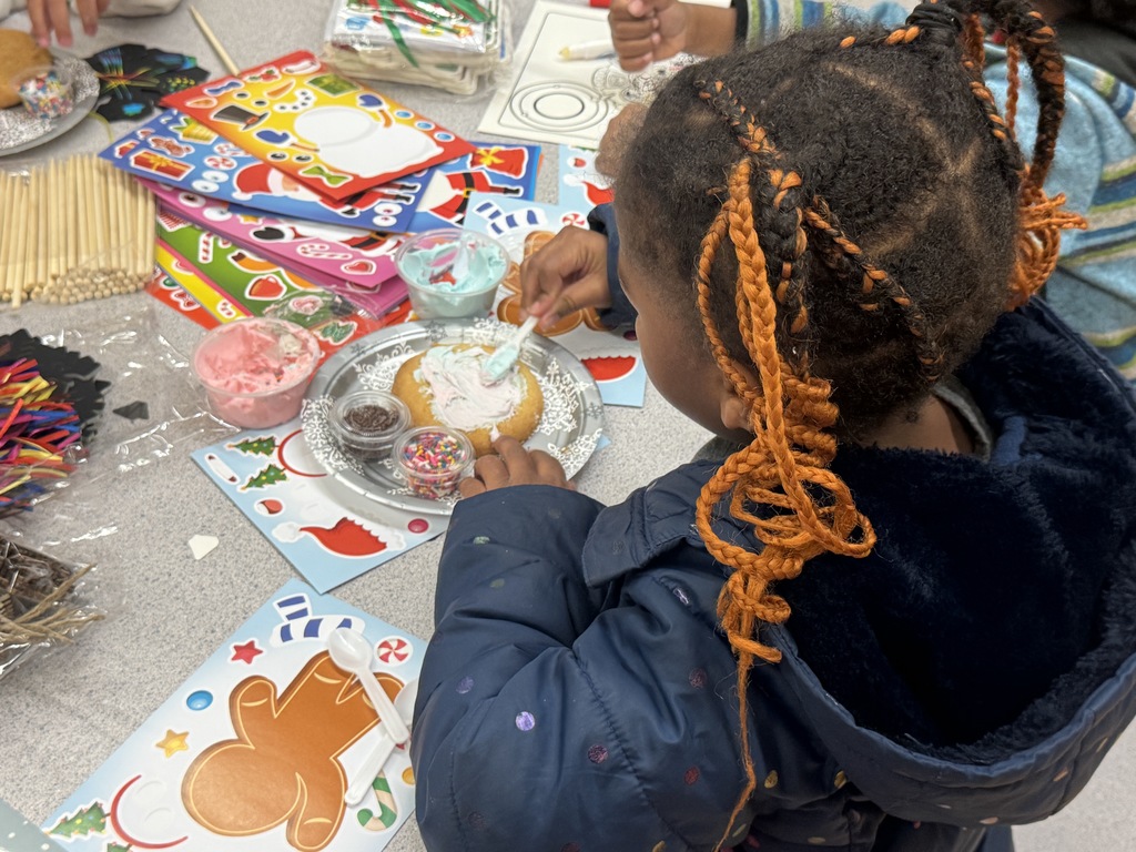 Village ECE student decorating sugar cookie with white icing and colorful sprinkles