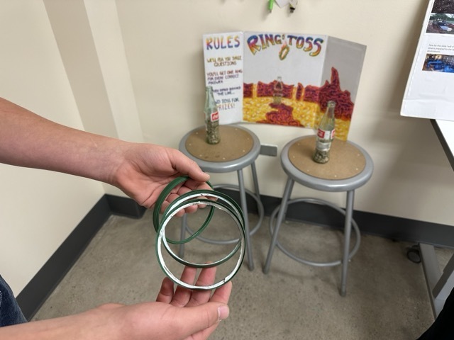 A close-up of a student’s hands holding three green rings for a "Ring Toss" game.