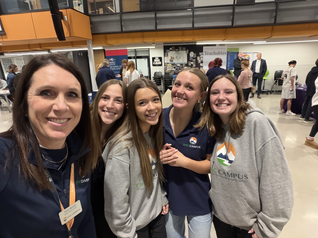A group selfie shows an EPIC Campus staff member and four high school students smiling at the camera. The students wear EPIC Campus shirts and hoodies with the mountain logo, and college fair booths and attendees are visible in the background.