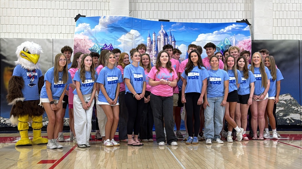 Students in Heritage Wish Week shirts pose with an eagle mascot in front of a Disney castle backdrop in a gymnasium.