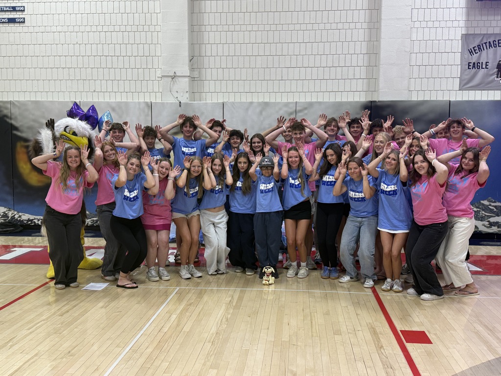 A large group of students in pink and blue Wish Week shirts pose with the eagle mascot while holding their hands up.