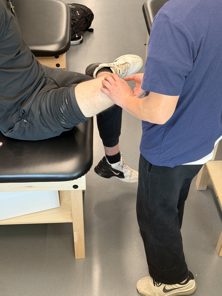 A person in a blue shirt stands near another person in black pants, both in a room.
