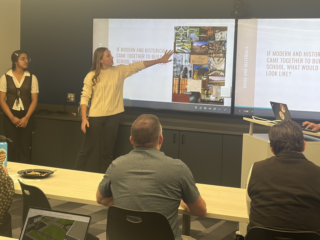 A woman presents a slideshow to a group in a classroom. The group sits in chairs facing a large screen.