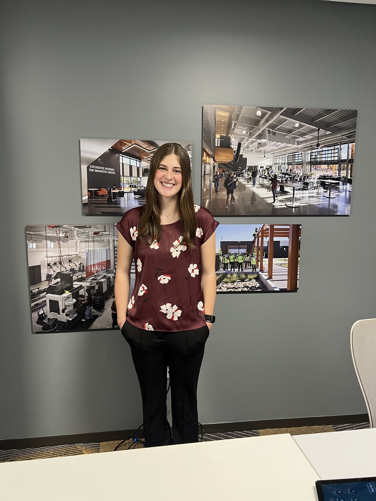 A woman wearing a maroon shirt with white floral prints stands with her hands in her pockets in an office.