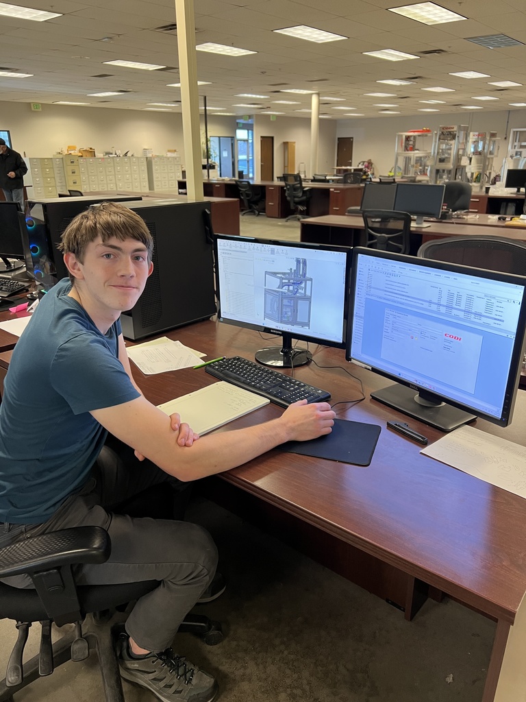 A man sits at a desk with a computer monitor displaying text, using a keyboard and mouse.