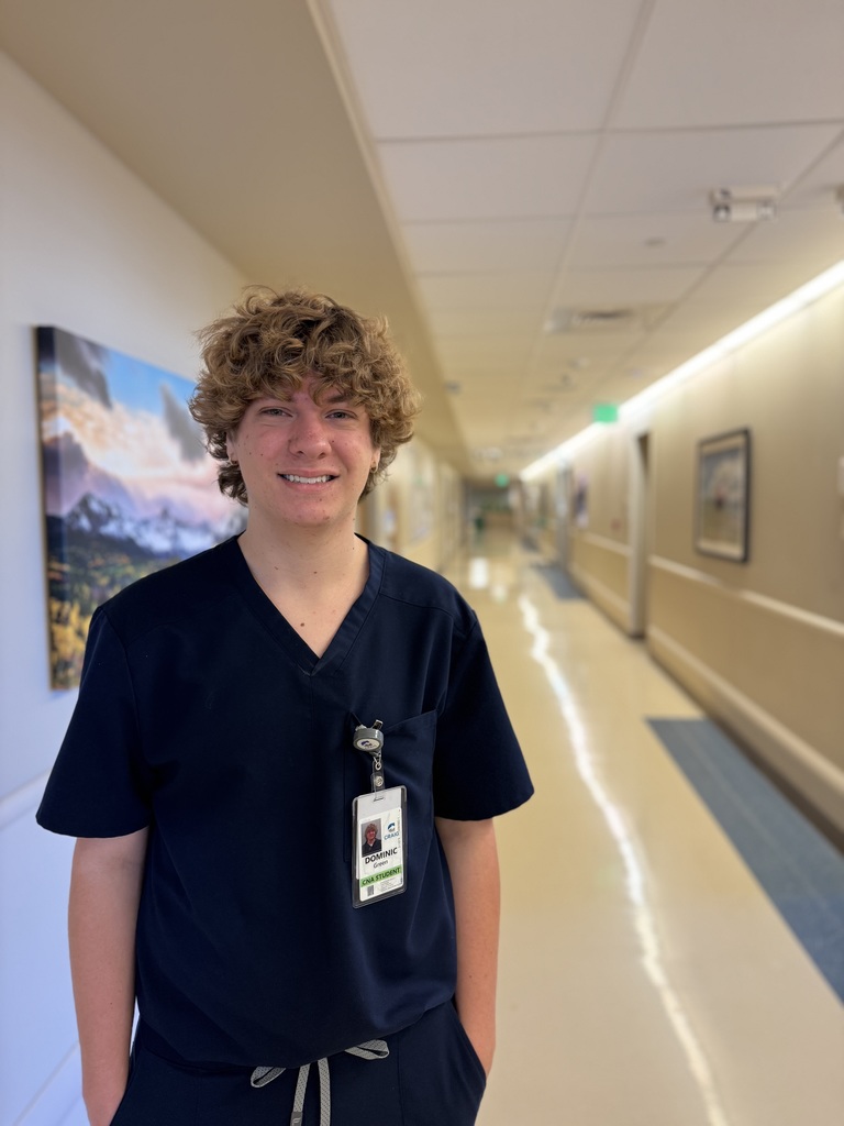 A man smiles at the camera, wearing a blue shirt, and an ID badge. He is in a hospital.