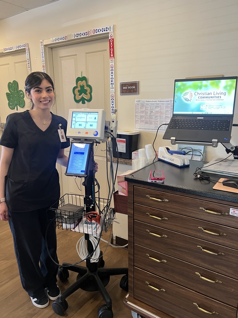A woman in black scrubs stands next to a medical cart with an IV pump and monitor.