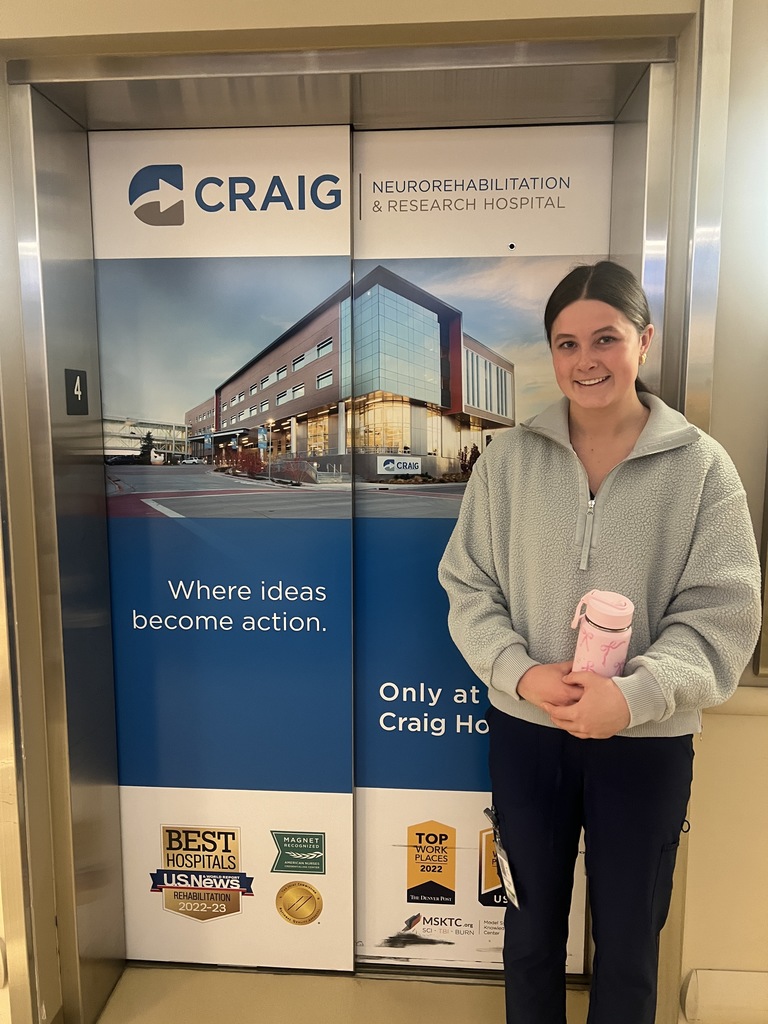 A woman stands in front of a large sign that reads "Craig" and holds a pink object.