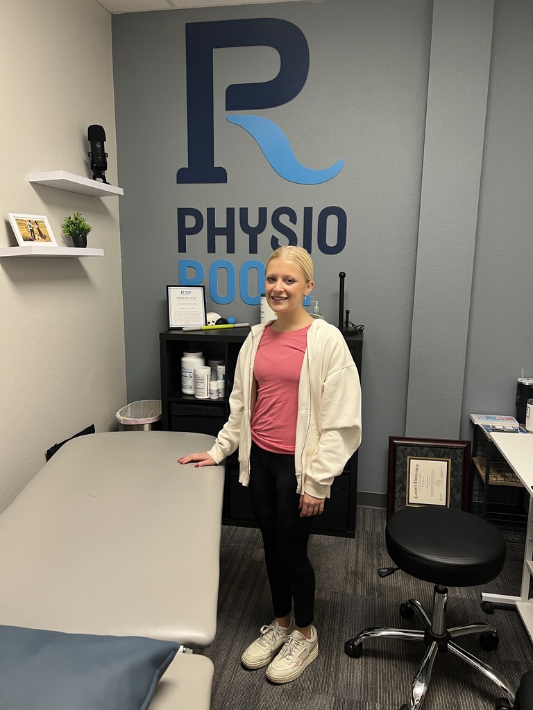 Person in pink shirt and white jacket stands in front of a wall with the letters R and Physio.