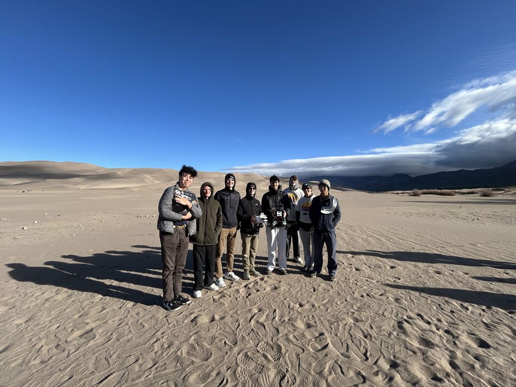 A group of people standing in a desert with dunes and a clear blue sky.