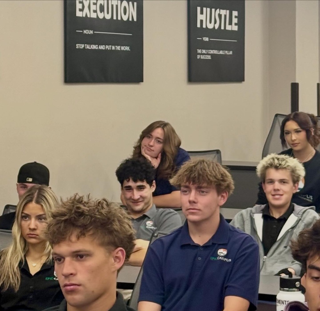 Group of people in a room, two posters on wall. Words "EXECUTION" and "HUSTLE" on black backgrounds.