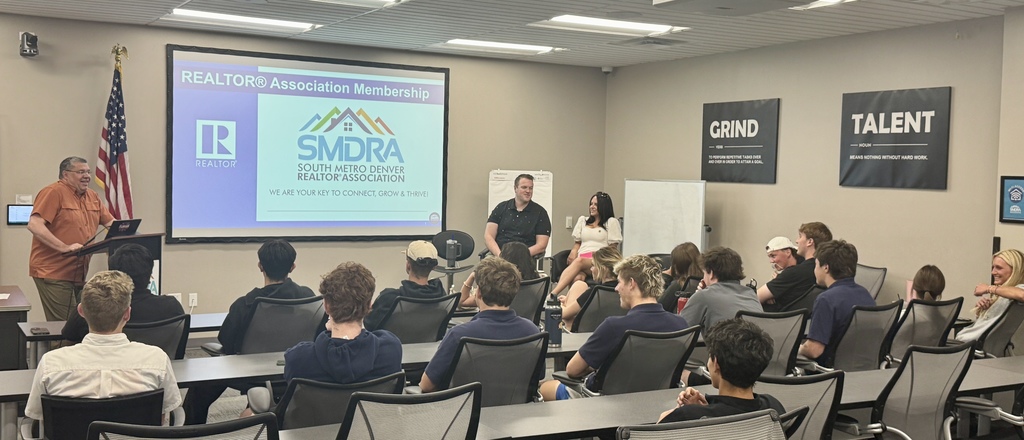 People in a classroom with a presentation on a screen. A flag on the left.