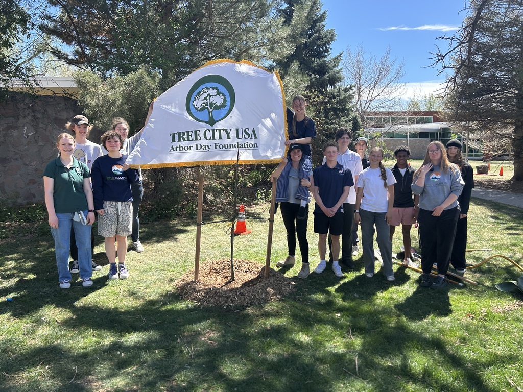 People stand behind a banner that says Tree City USA, near a tree. Trees and a building are in the background.