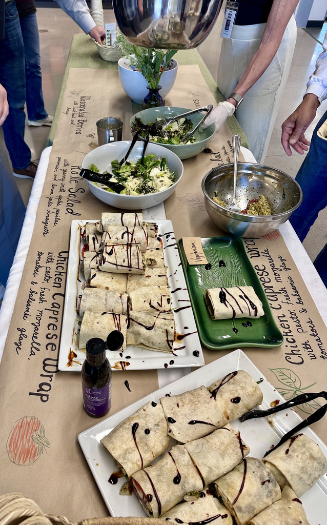 A table displays various food items, including burritos, salad, and a bottle of sauce. The table is covered with a brown cloth.