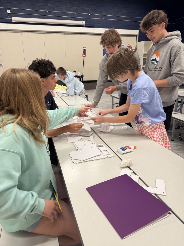 A group of students work together at a table in a classroom, sorting and examining pieces of paper.