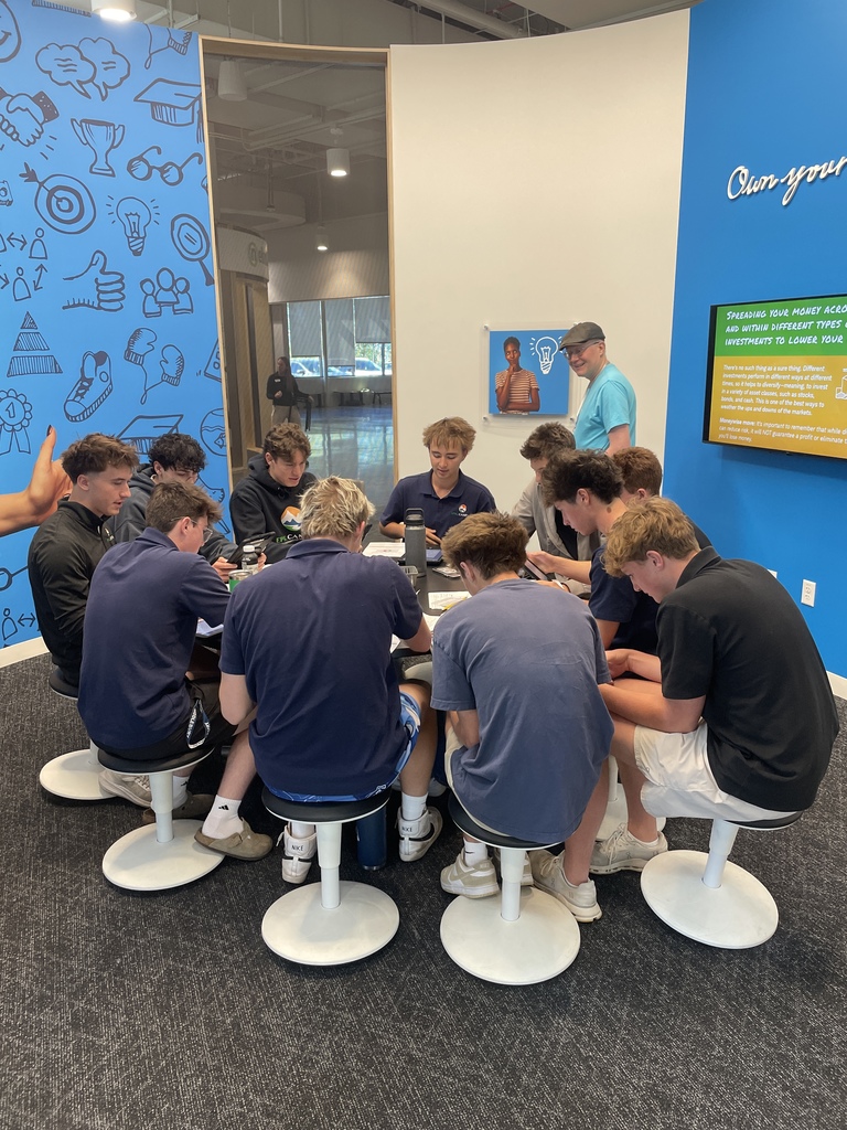 A group of young men seated around a table in a room with blue walls and a sign.
