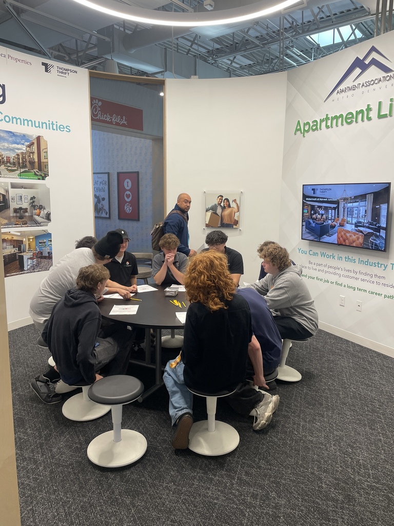 People sit around a table in a meeting room with a TV screen on the wall and artwork.
