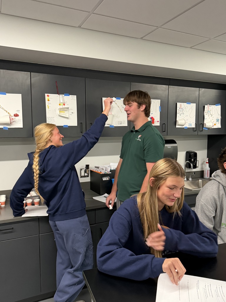 A group of people in a lab, a woman pointing to a paper while two others look on.