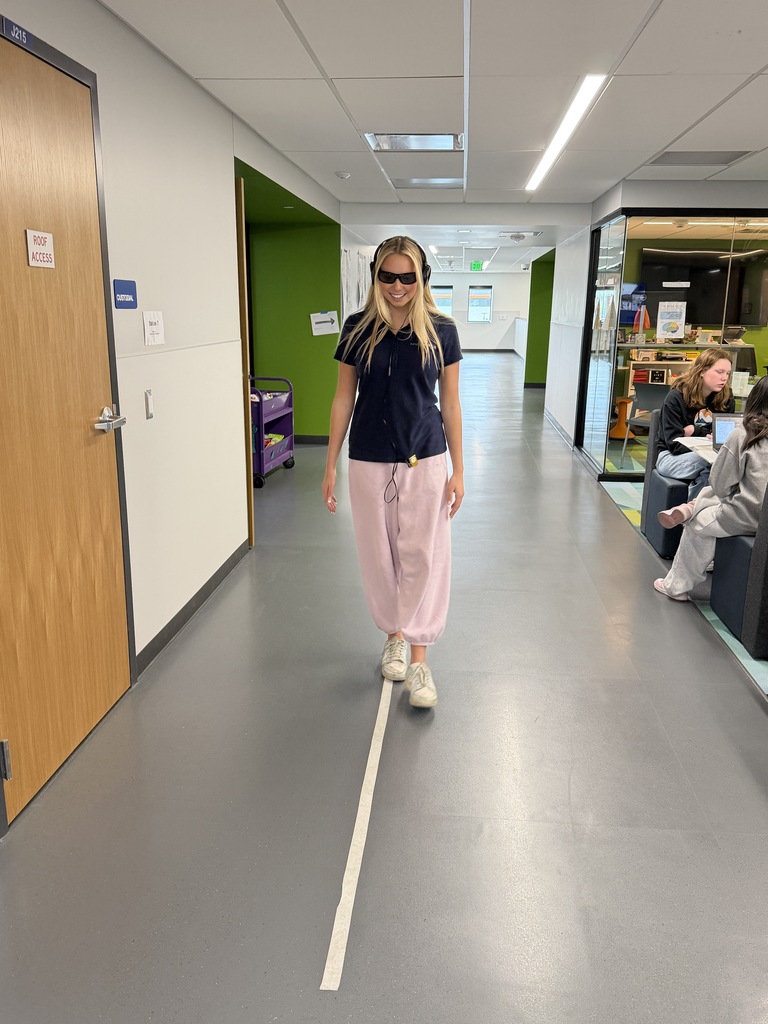 Person with sunglasses and headphones walking on a white line in a long, open corridor.